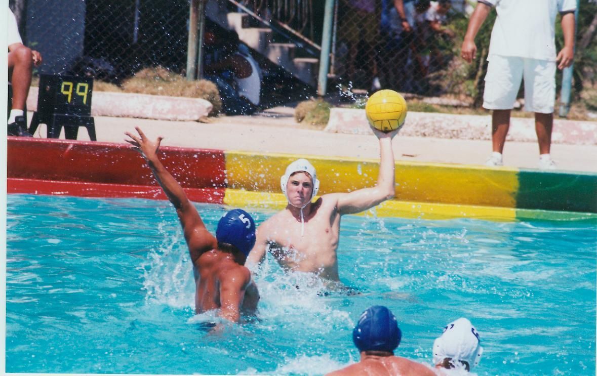 Water polo game in a pool; player throws yellow ball. Others in blue caps attempt to block.