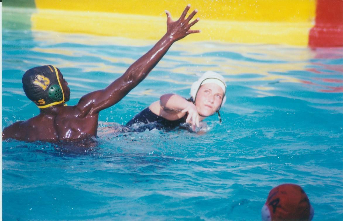 Water polo players in a pool, one reaching up to block, other swimming forward.