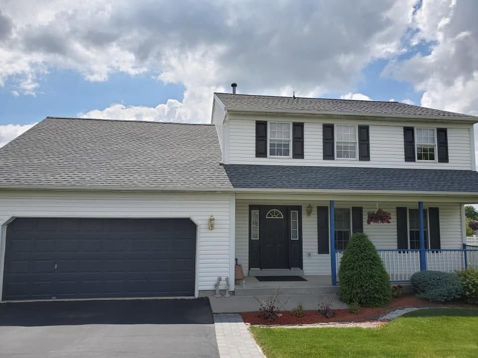Two-story suburban house with gray siding, white trim, and a dark garage door under a cloudy sky