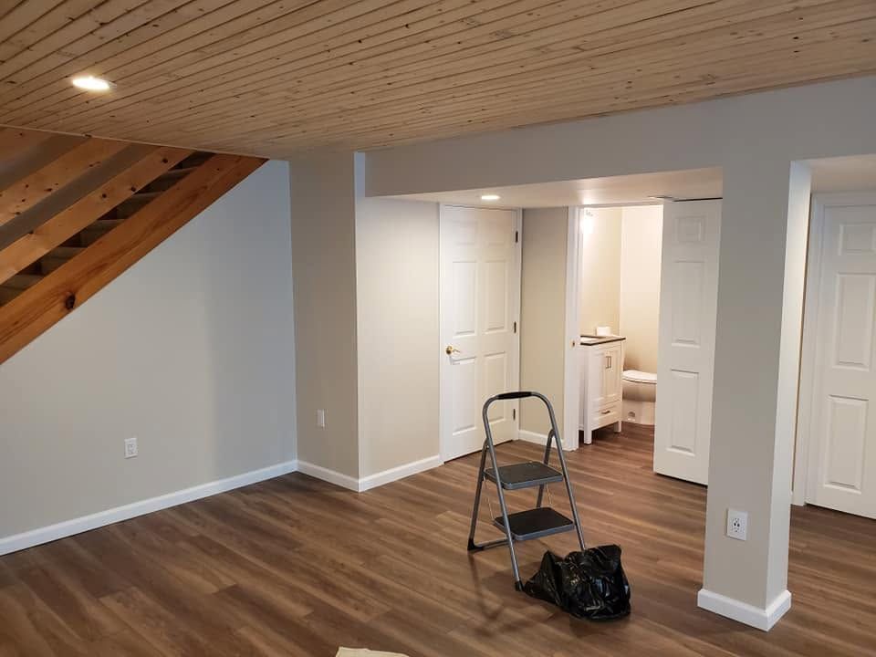 Empty basement room with wood floors, sloped wood ceiling, and step ladder near a doorway under renovation