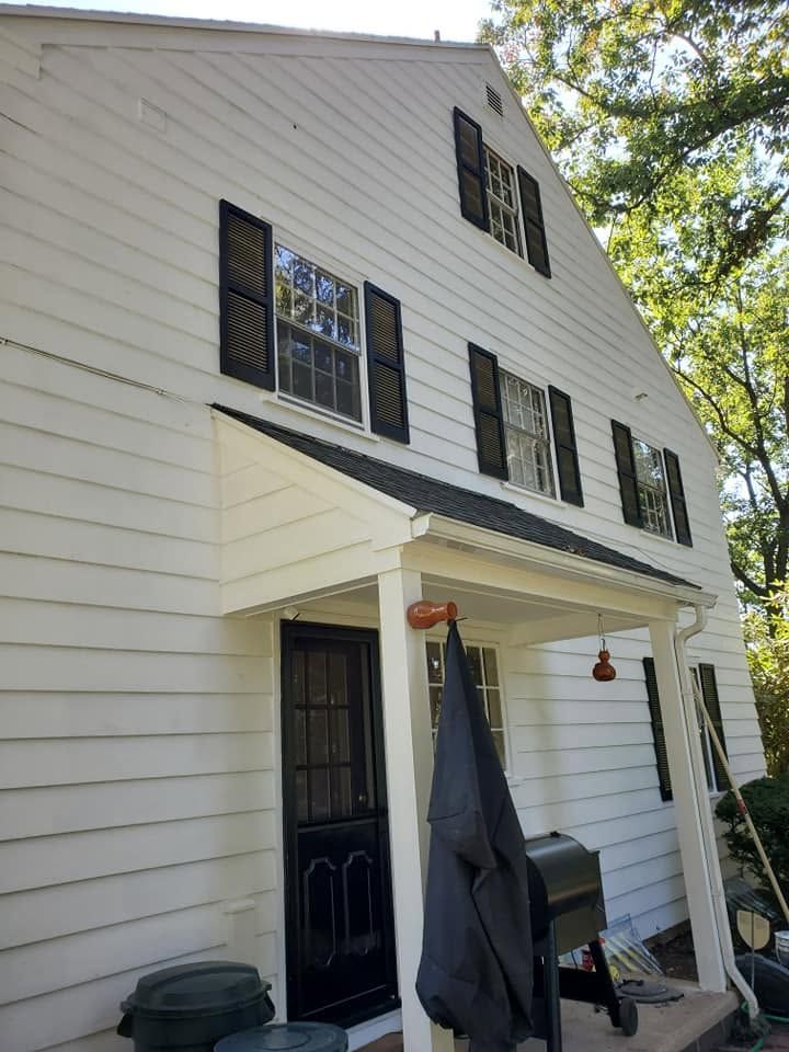 White house exterior with black shutters, front door, porch awning, and hanging patio umbrella