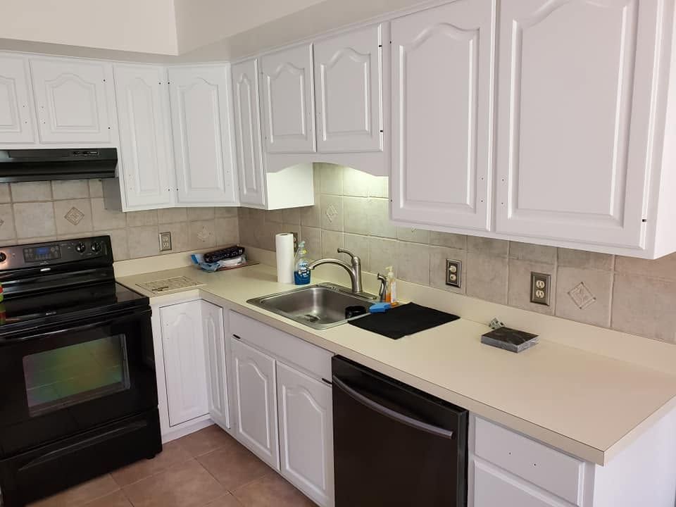 White kitchen with black stove and dishwasher, beige countertops, and sink under cabinets