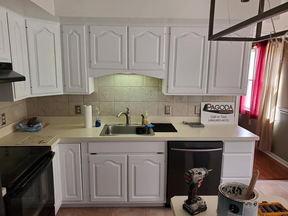 Small kitchen with white cabinets, beige countertops, black appliances, and a red-curtained window.