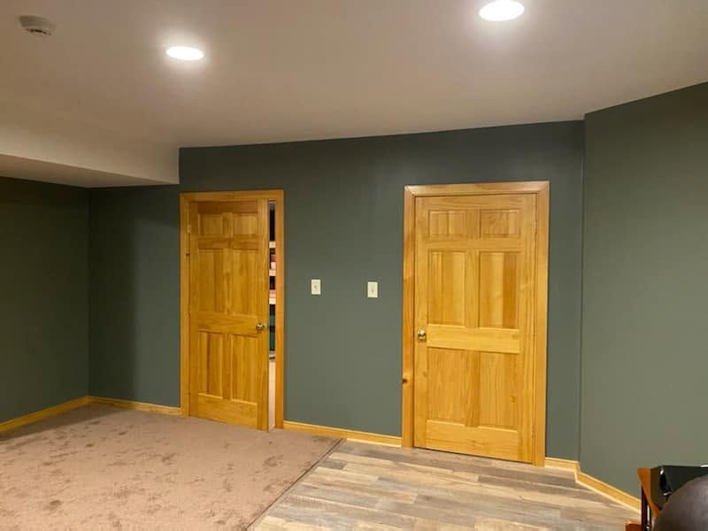 Empty room with dark green walls, two wooden doors, recessed lights, and carpeted floor.