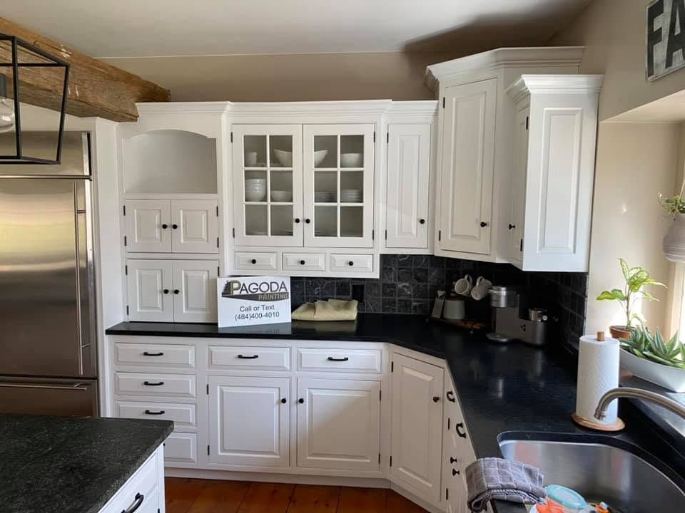 Bright white kitchen with black countertops, stainless fridge, and a small sign by the sink