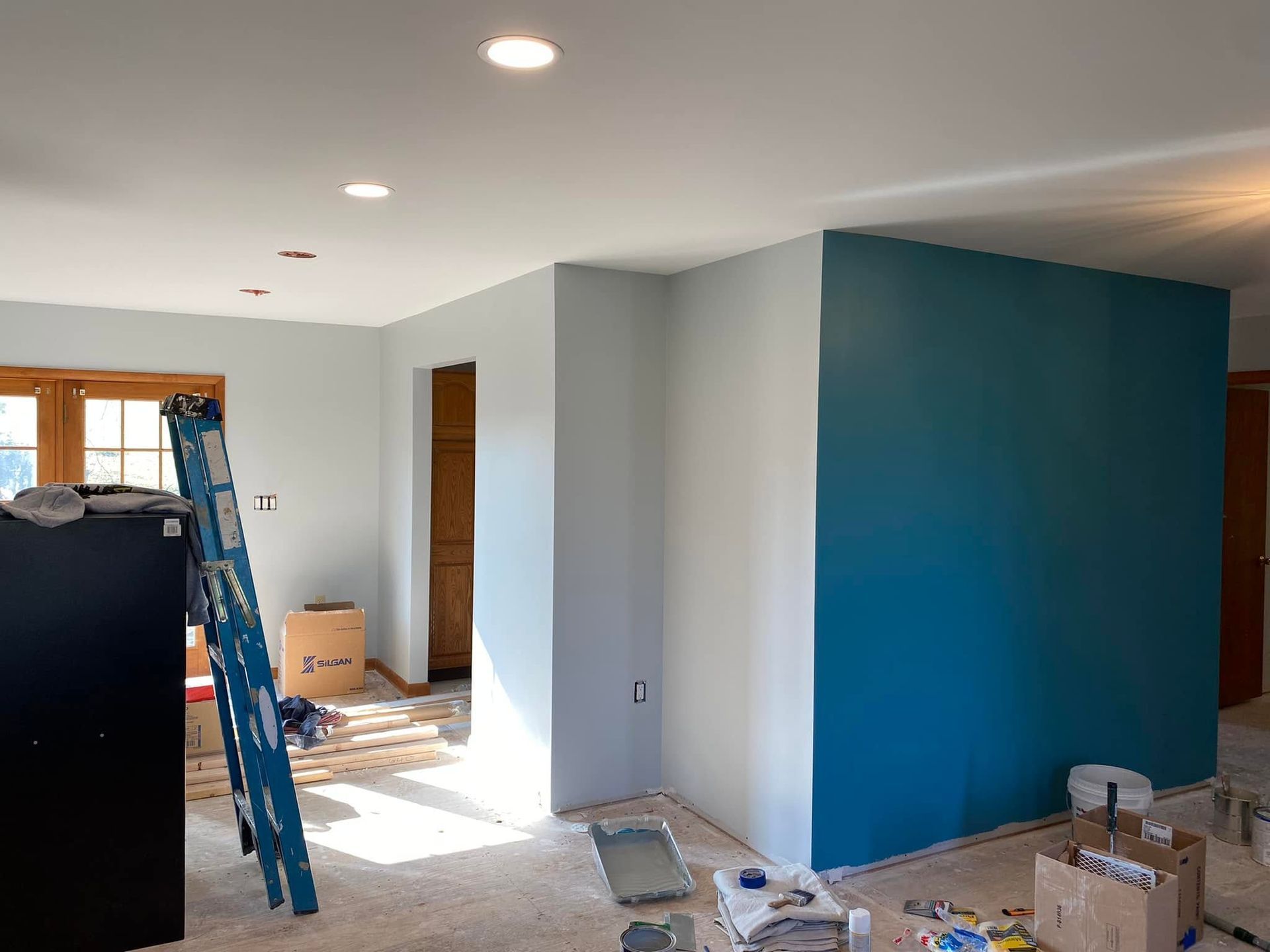 Partially renovated room with teal accent wall, ladder, and boxes in daylight