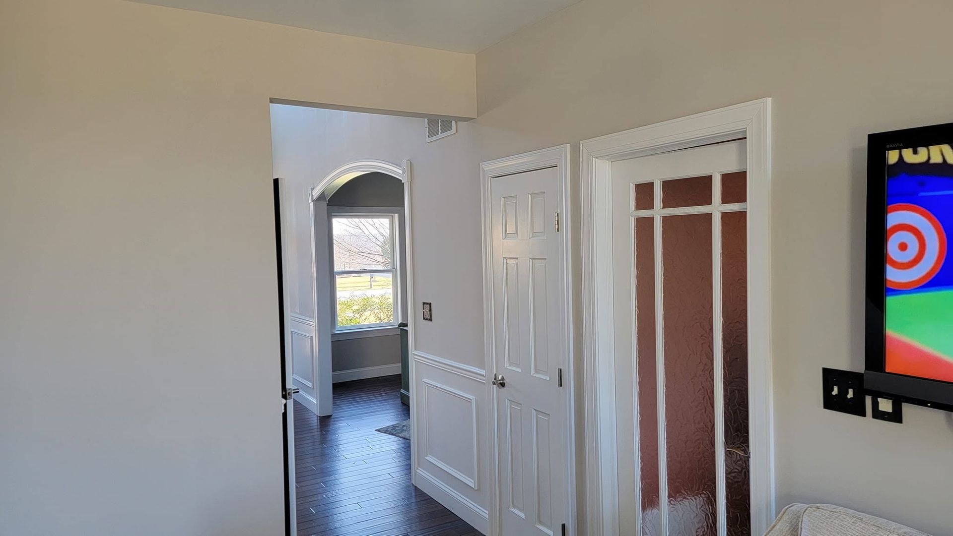 Bright room with open white doors, tiled floor, and a wall-mounted TV on the right.