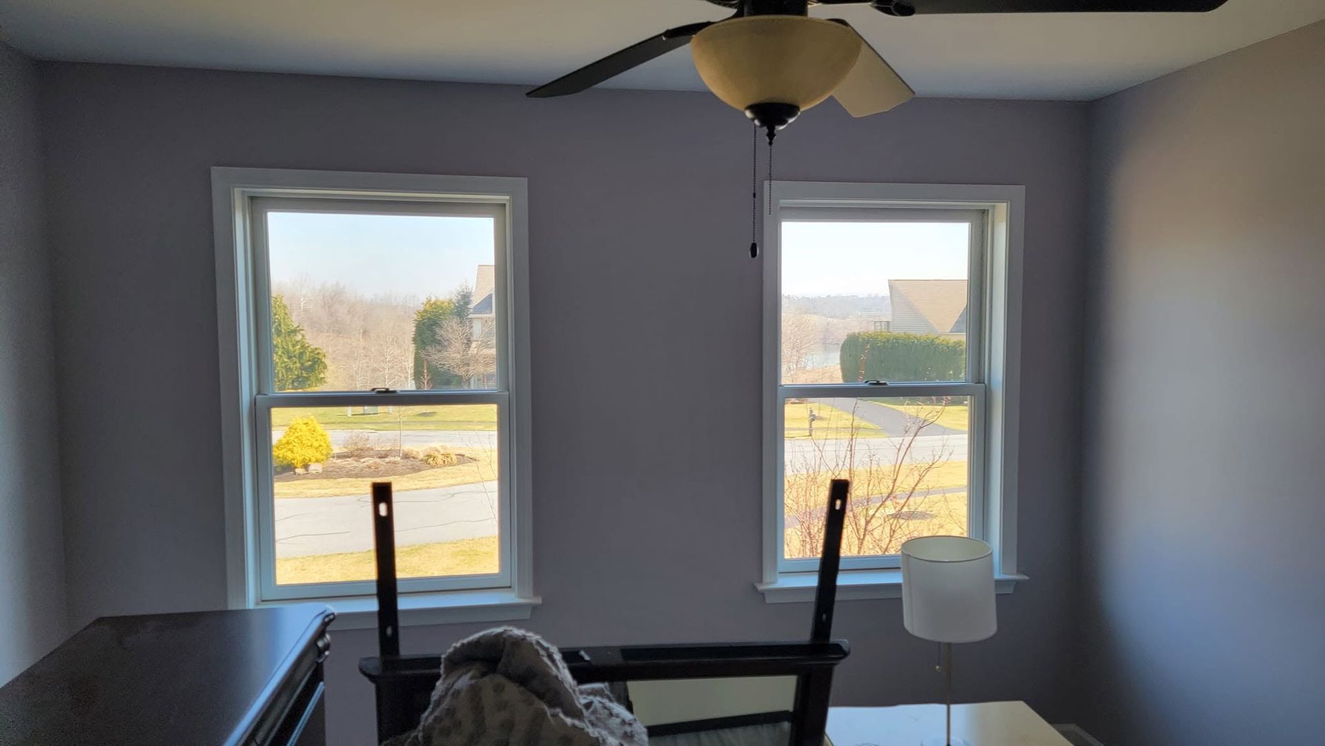 Bedroom with two windows, a ceiling fan, and a bed in the foreground, lit by daylight.