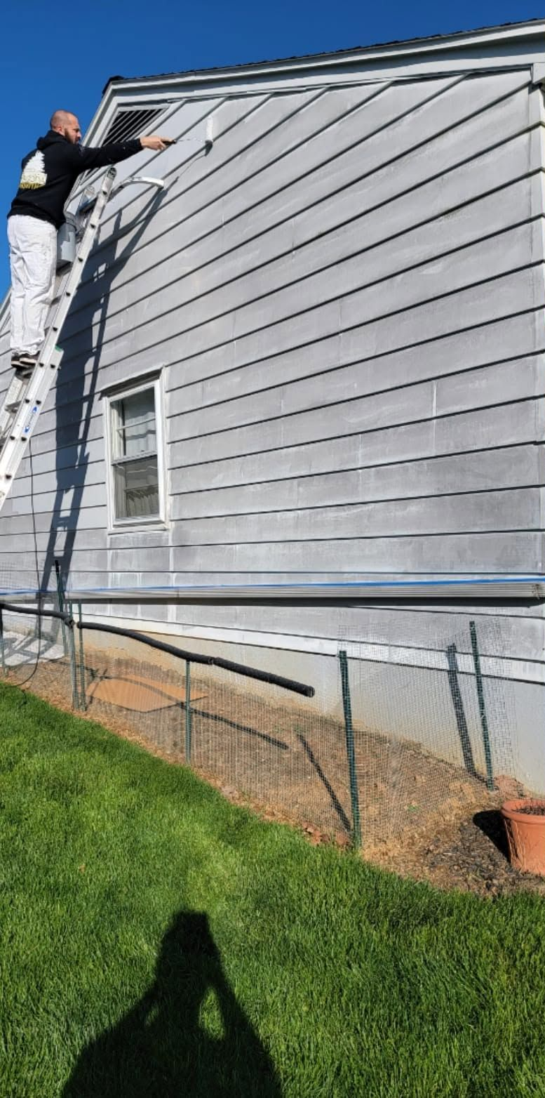 Person on a ladder painting gray siding on a house exterior.