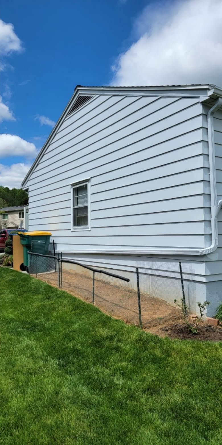 Light blue vinyl-sided house exterior with a grassy yard and downspout over a concrete basement wall