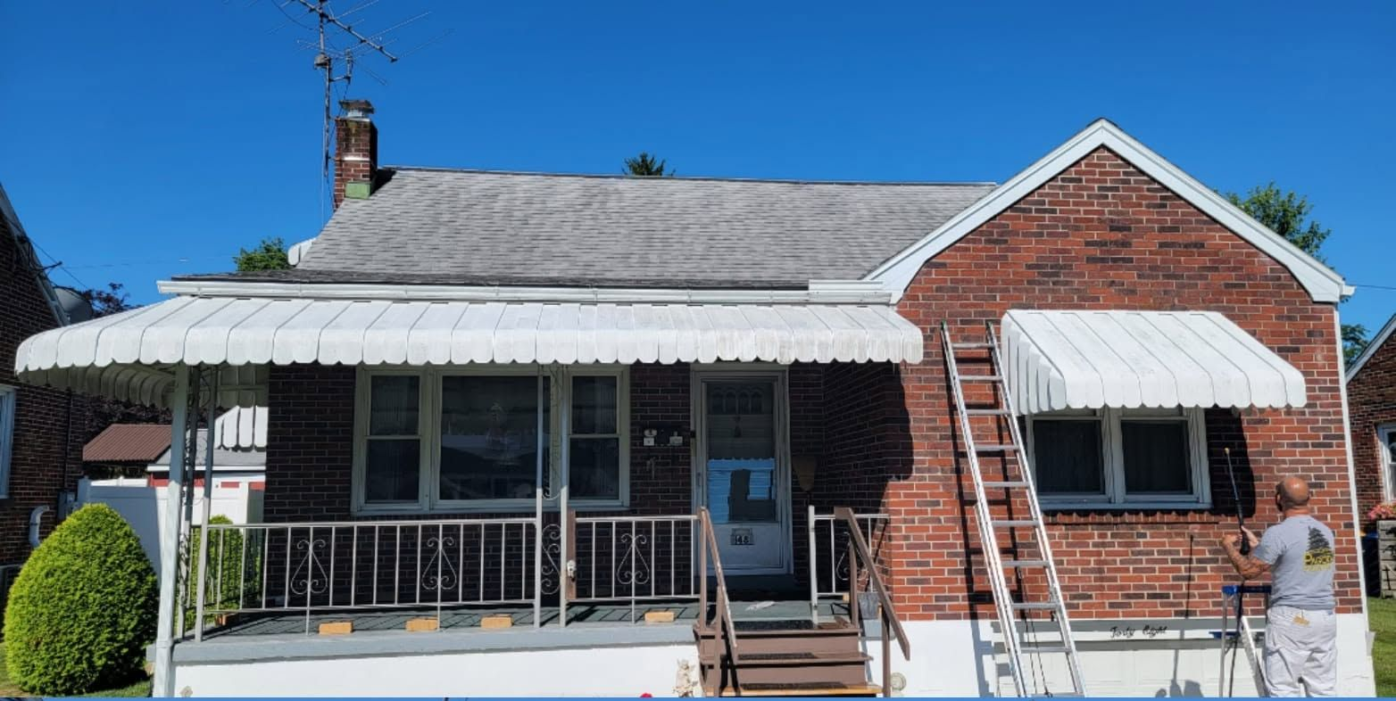Brick house with white awnings, a front porch, and a small lawn under a clear blue sky