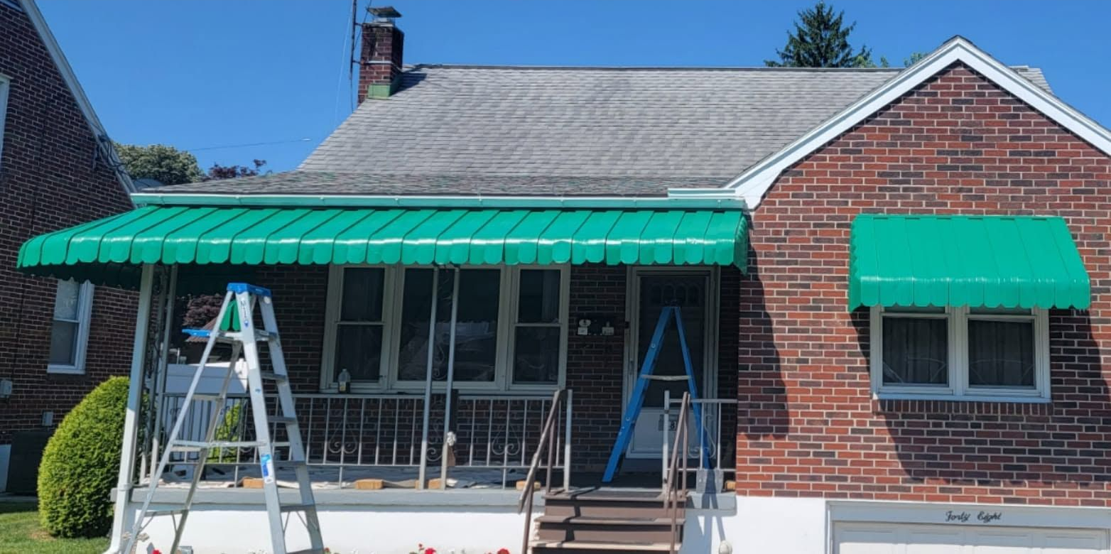 Brick house with green awnings and two ladders set up in front during exterior work