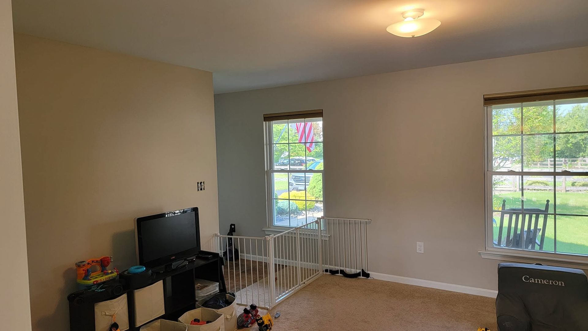 Living room with TV, white table and chairs, two windows, and a view of a patio outside