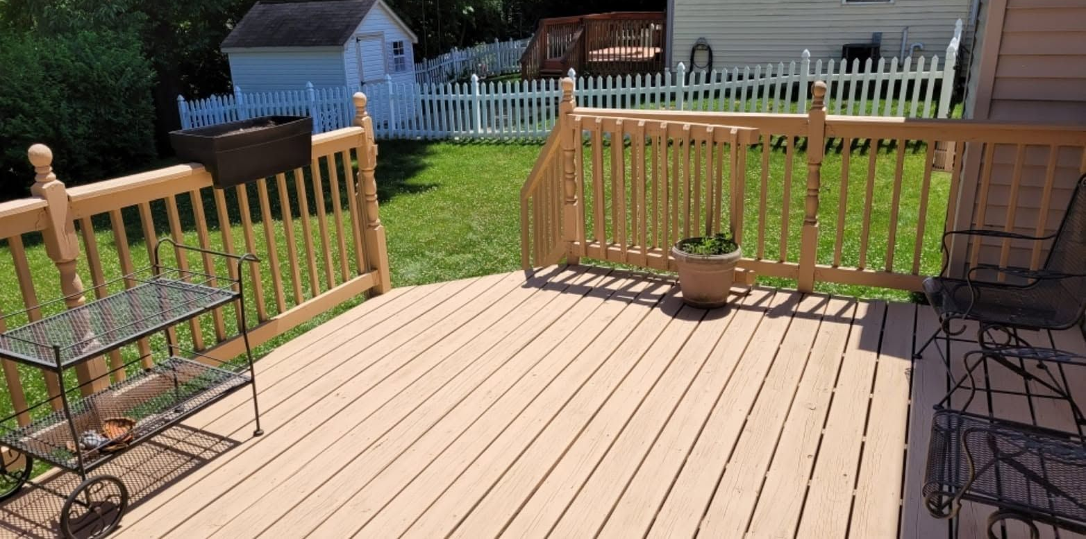 Wooden backyard deck with railing, chairs, and a grassy yard with a small shed beyond the fence