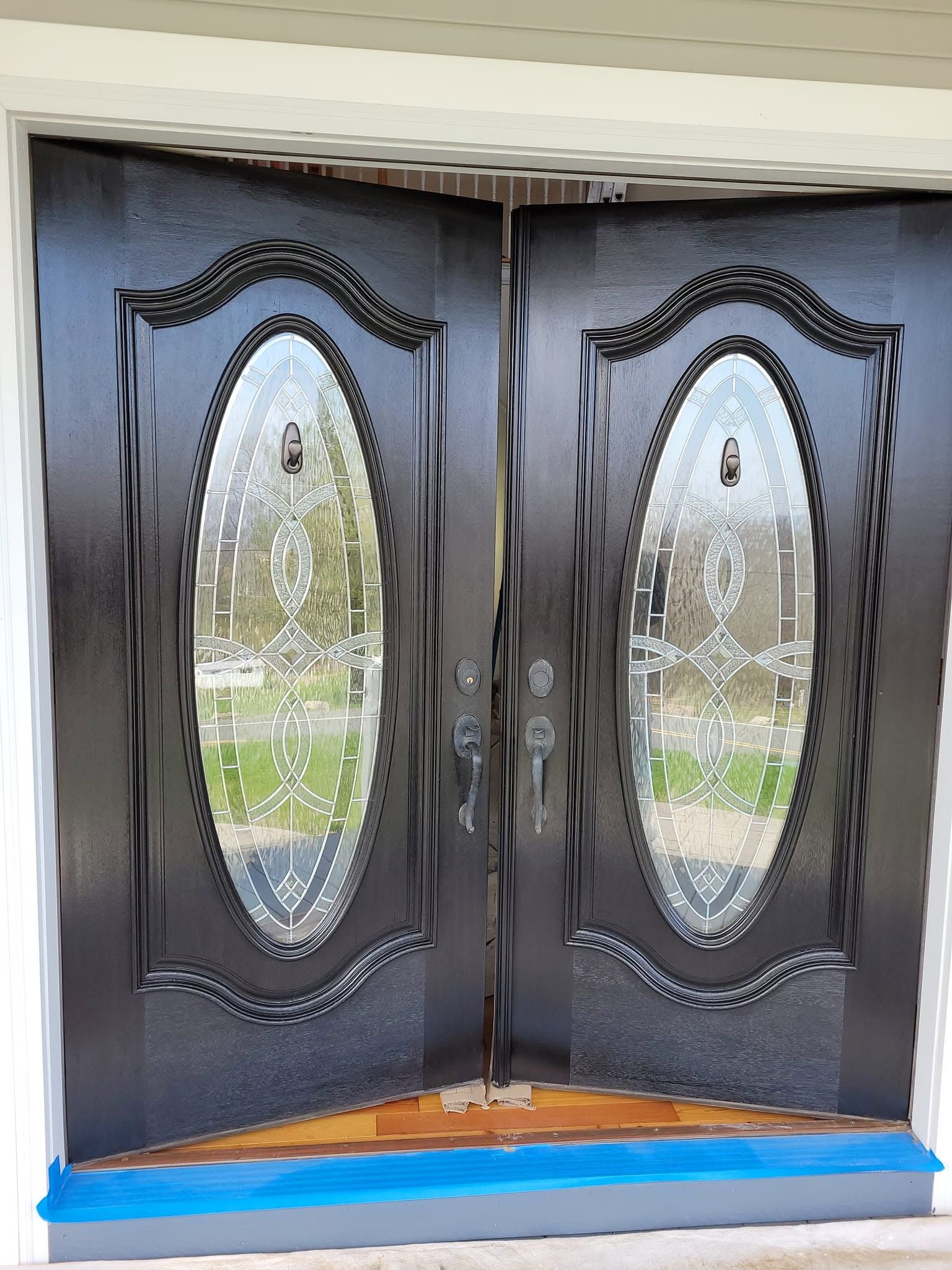Black double front doors with oval glass panels and ornate trim, viewed from outside on a blue step.