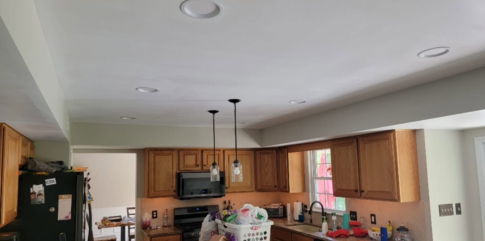 Kitchen interior with wooden cabinets, island, pendant lights, and countertop clutter.