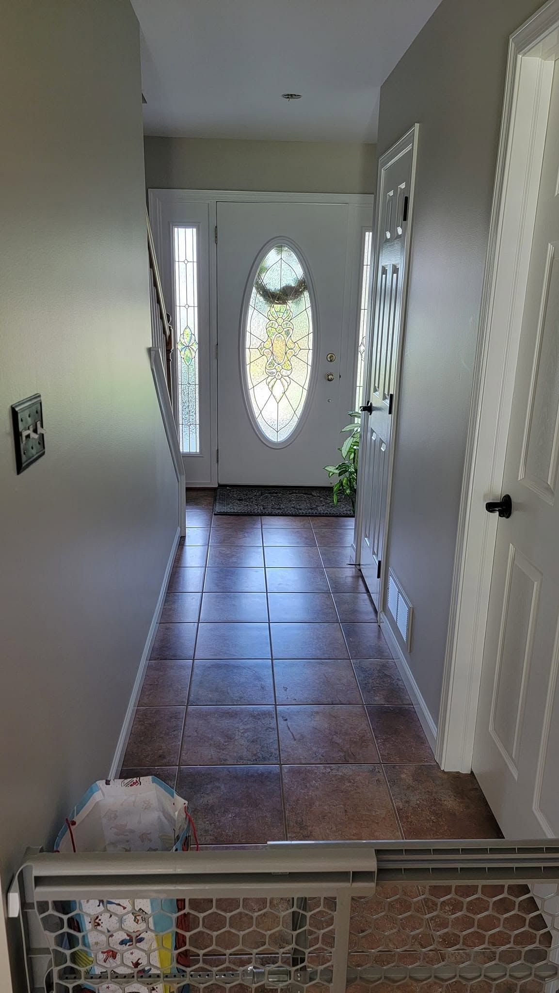 Narrow hallway with tiled floor, white walls, and a front door with an oval glass window.