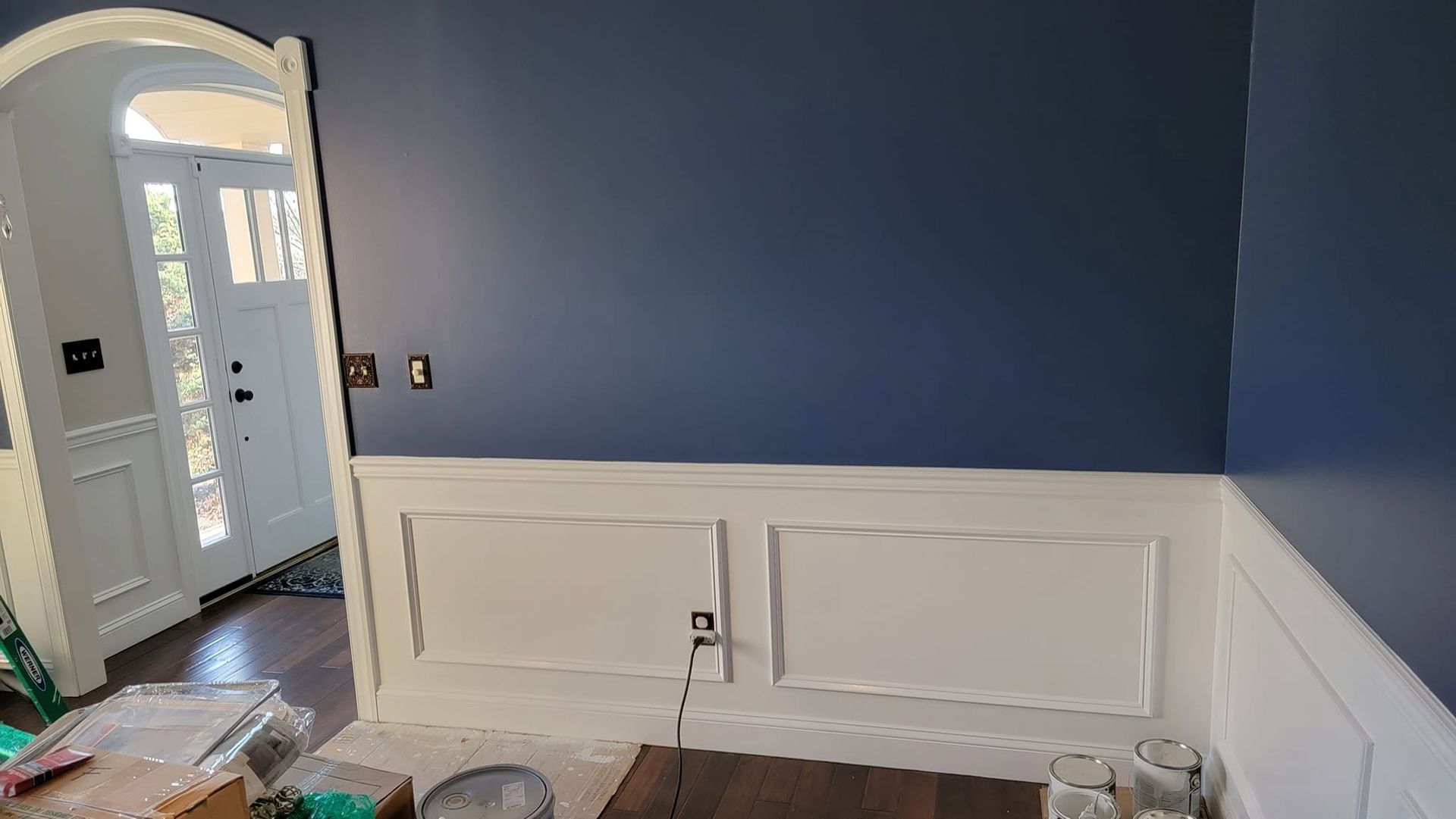 Empty room with navy blue walls, white wainscoting, and an open front door.