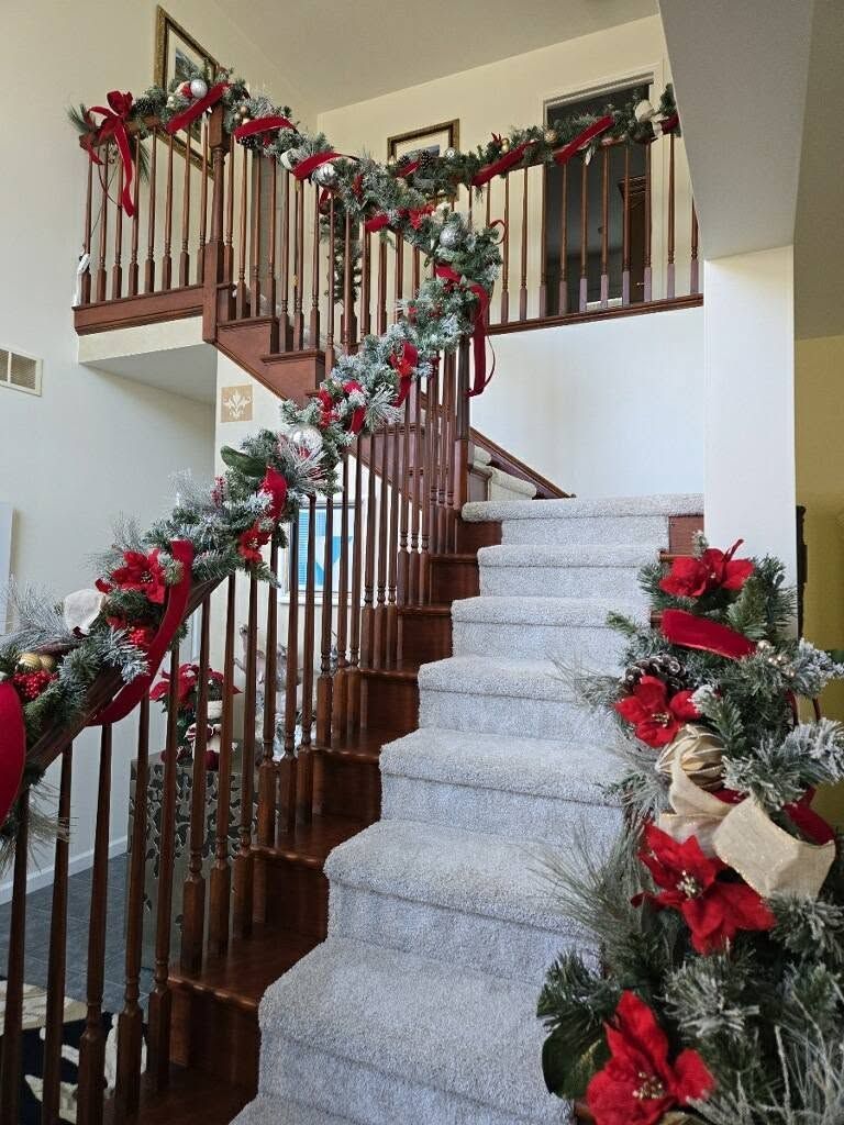 Holiday garland and red bows decorate a carpeted staircase with wooden railing and balcony.