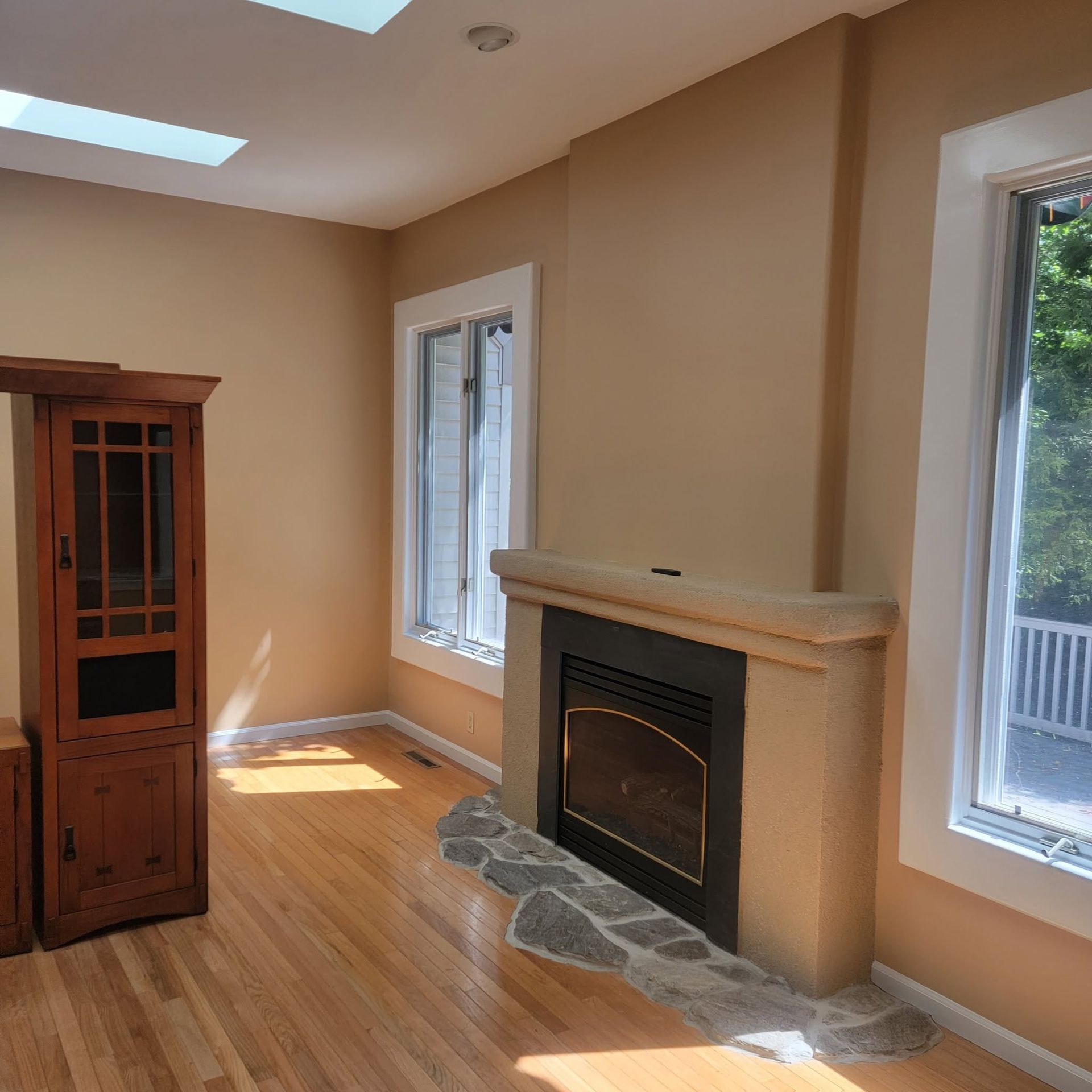 Empty living room with hardwood floors, beige walls, a fireplace, and two windows letting in daylight