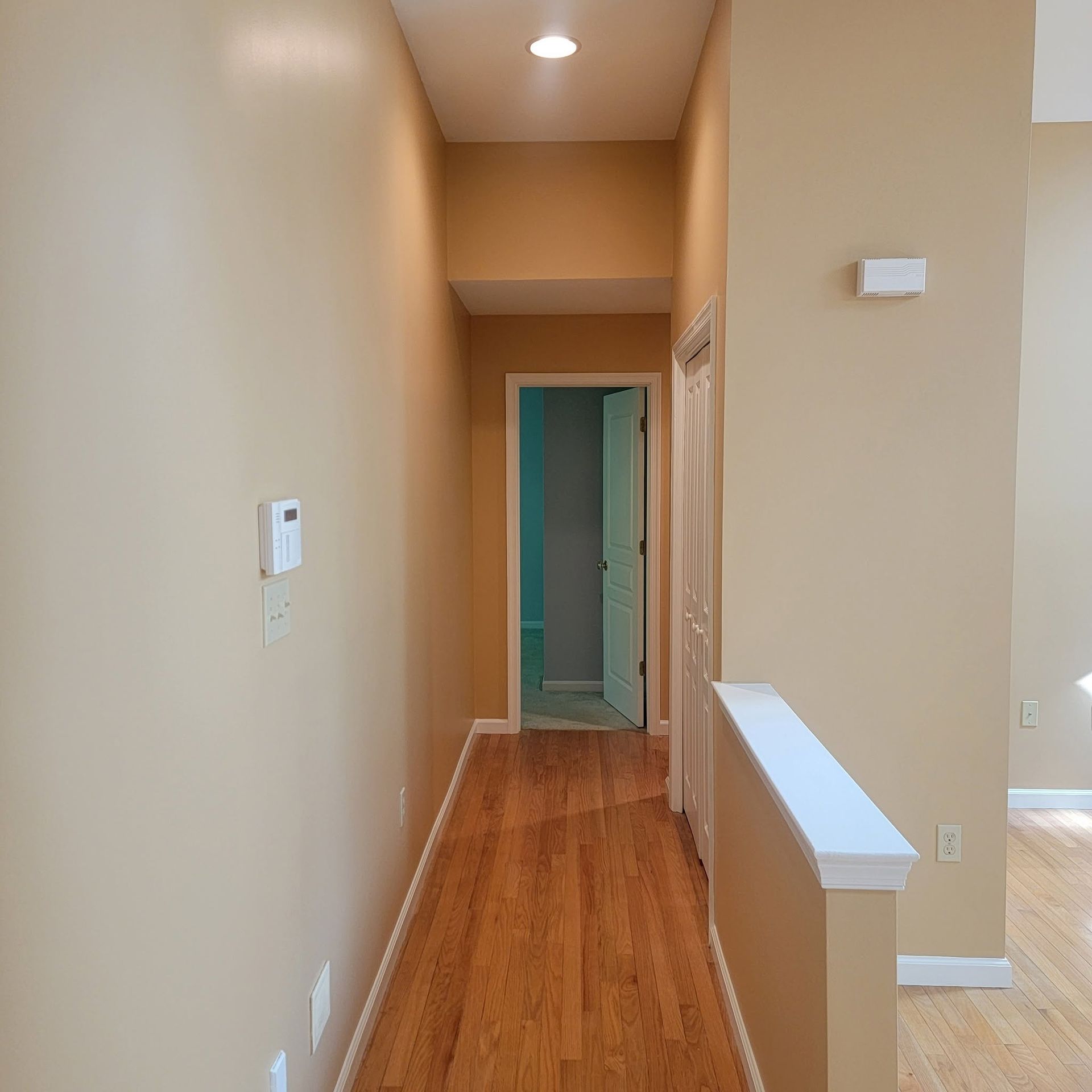 Empty beige hallway with hardwood floors, white trim, and a doorway at the far end
