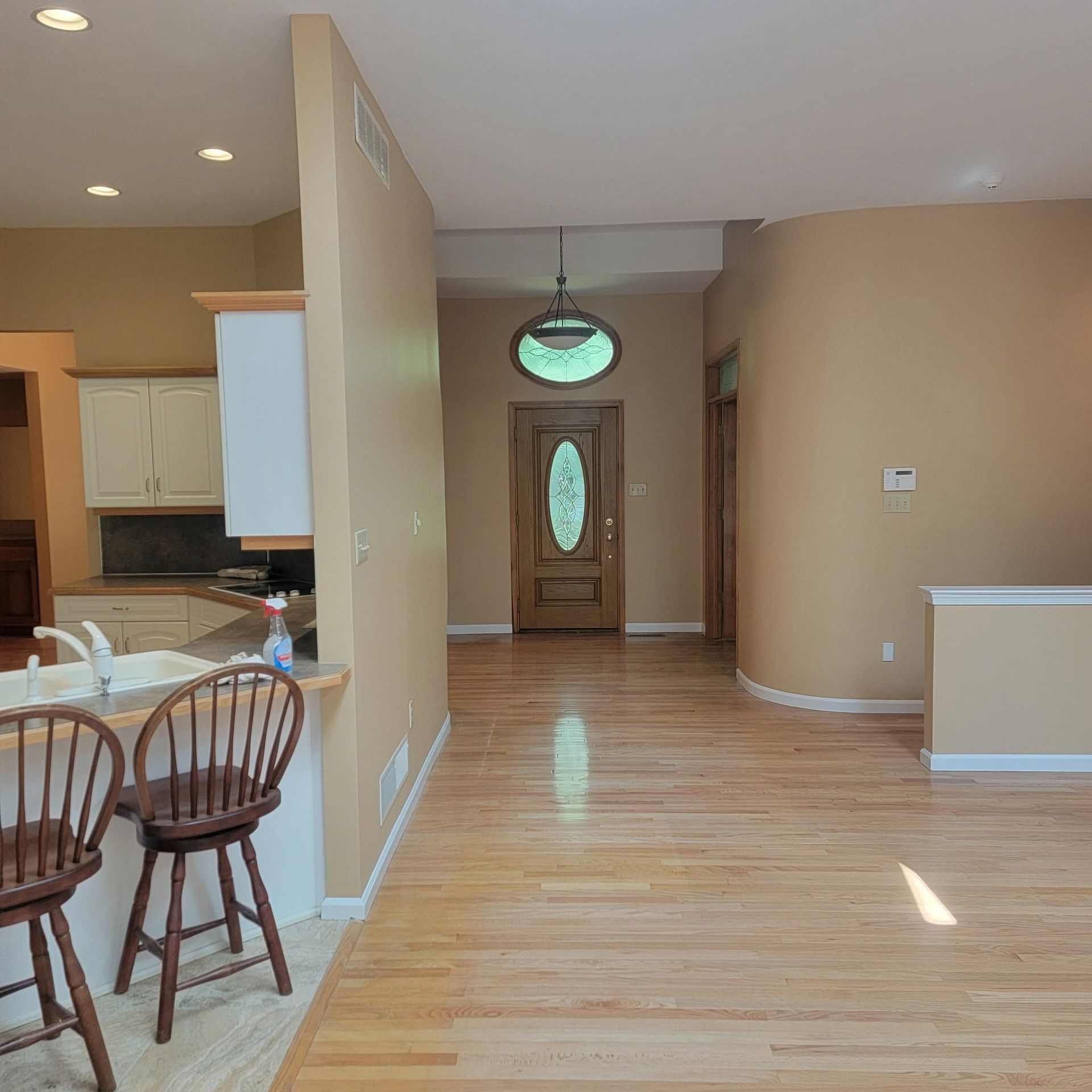 Empty beige dining and living area with hardwood floors, kitchen bar stools, and a front door visible in back