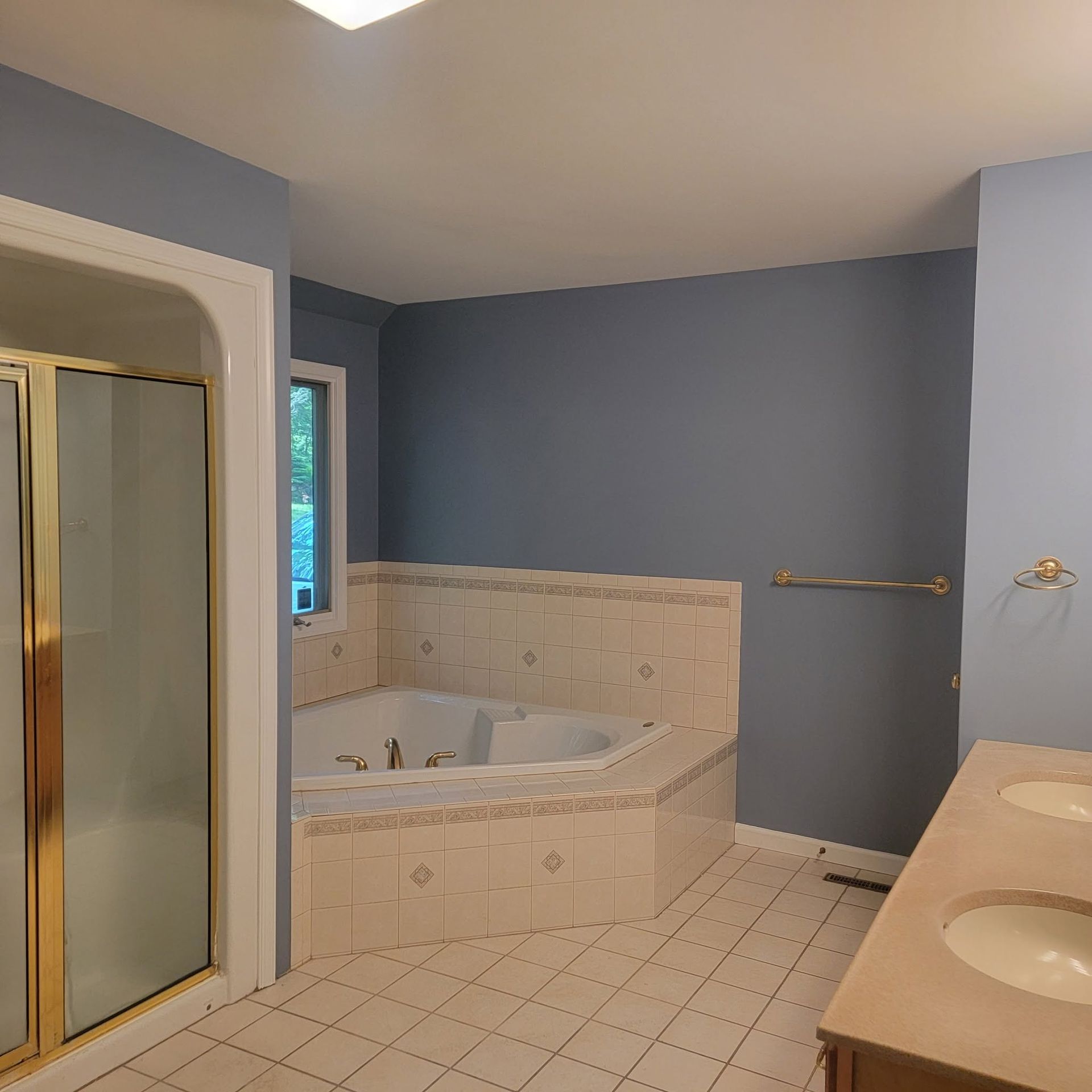 Blue bathroom with tiled corner bathtub, glass shower, and beige vanity countertops