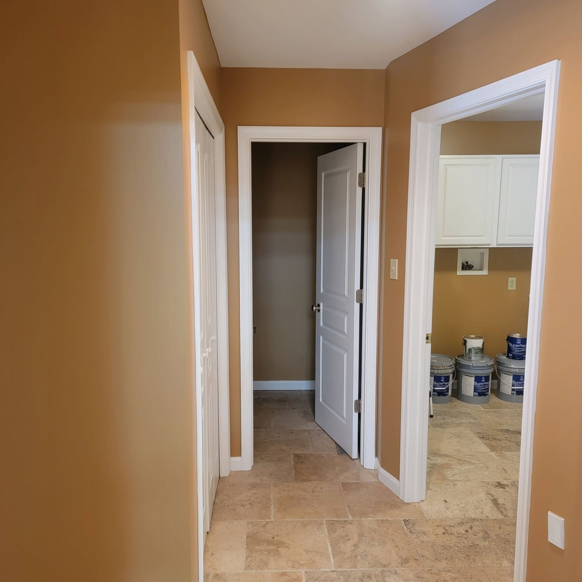Hallway with tan walls and tile floor, open white doors, leading to a laundry or utility room.