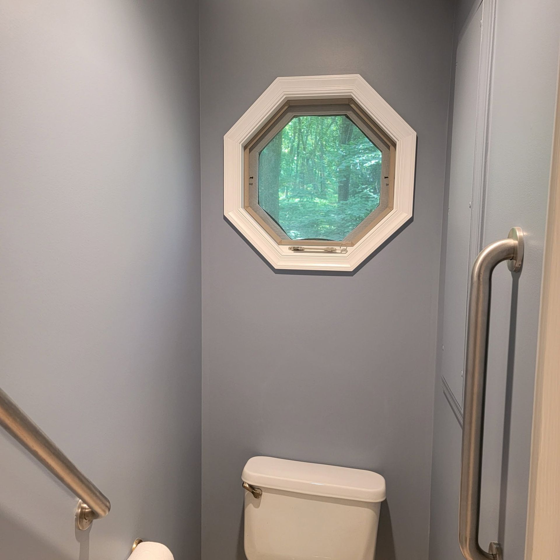 Narrow gray stairwell with a small octagonal window and a toilet at the bottom landing