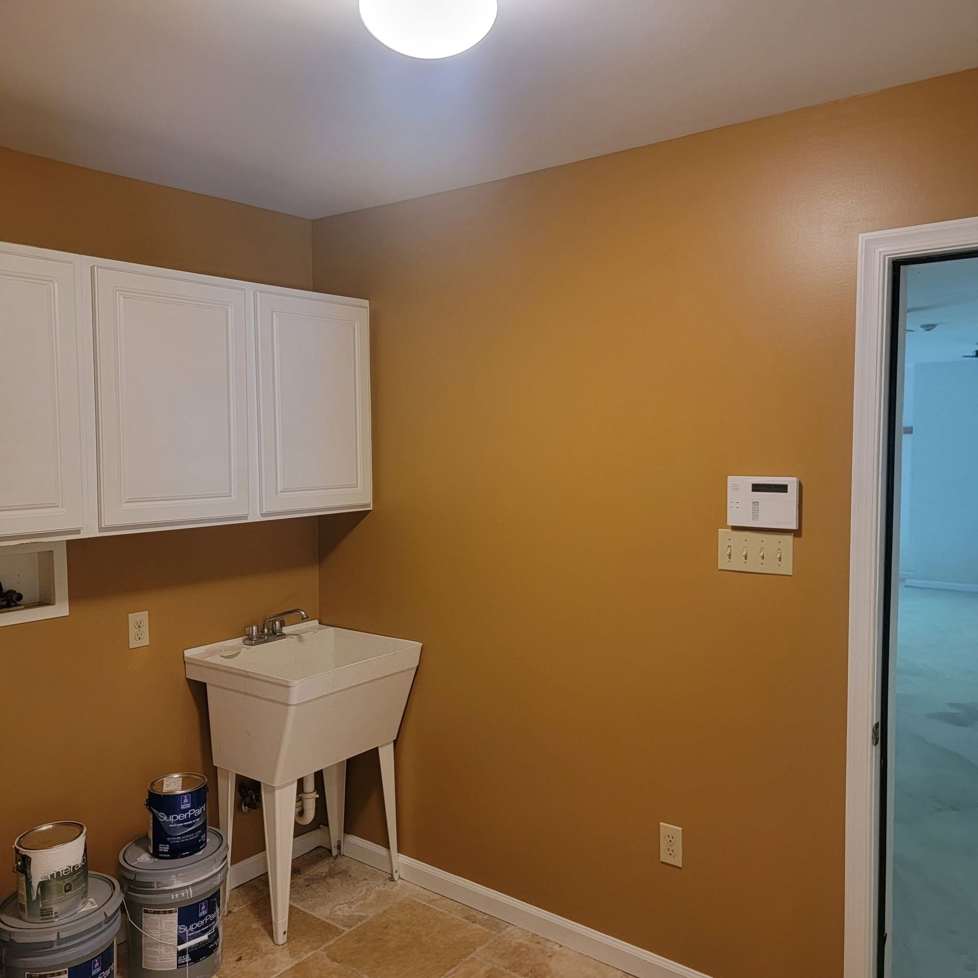 Laundry room with white cabinets, utility sink, mustard walls, and paint cans on the floor