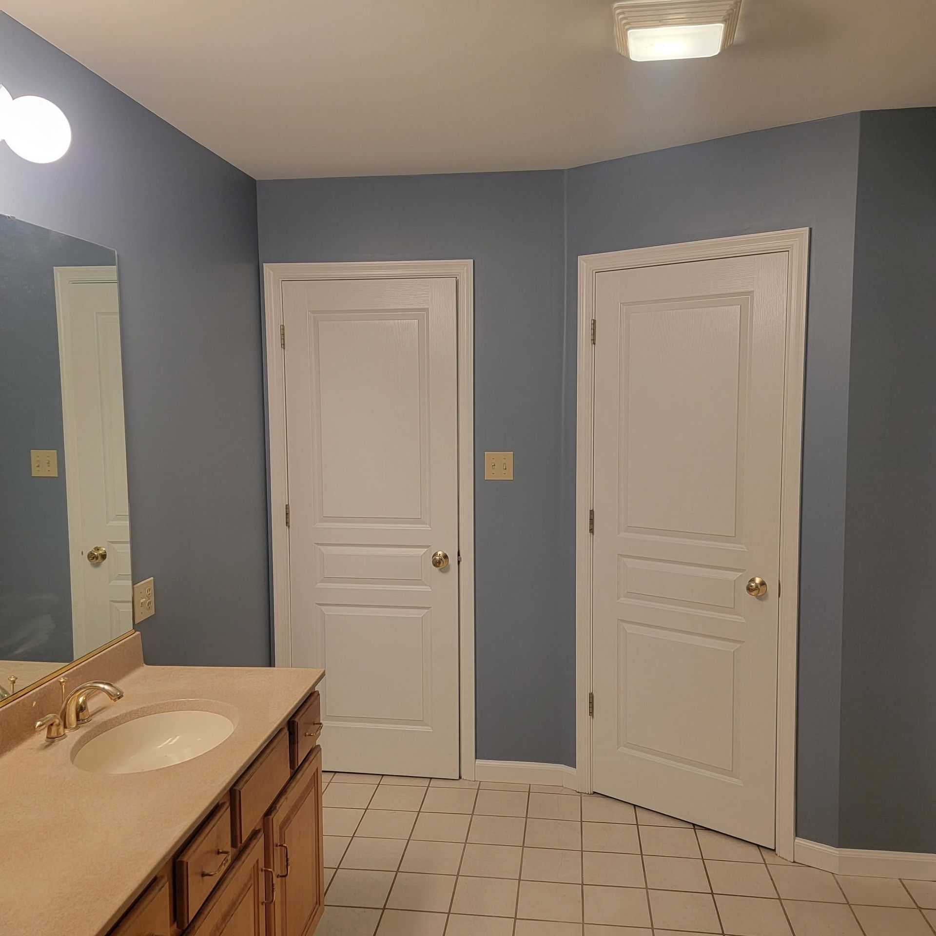 Bathroom with blue walls, white doors, tiled floor, and a vanity with sink and mirror.
