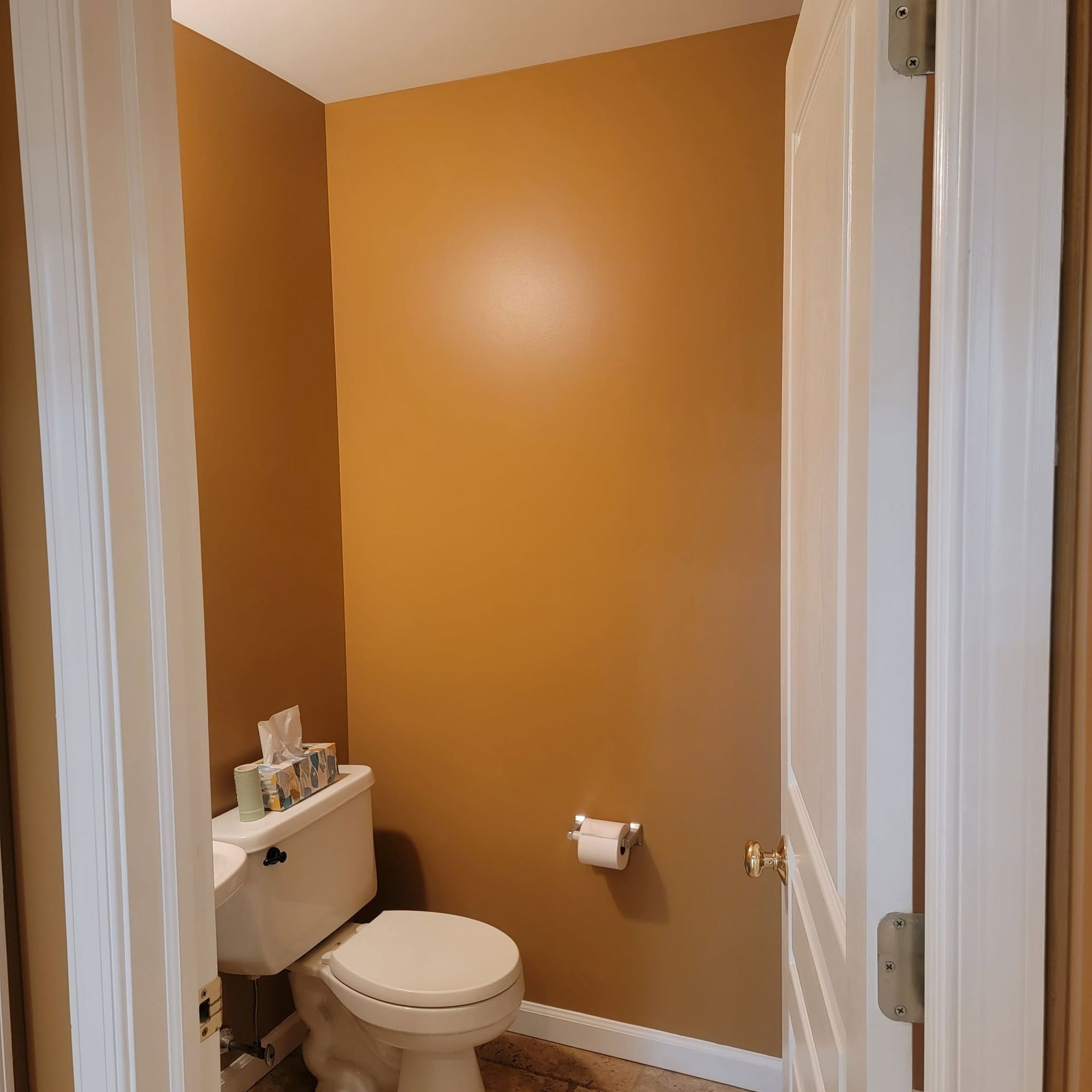 Small bathroom with orange walls, white toilet, and toilet paper holder.