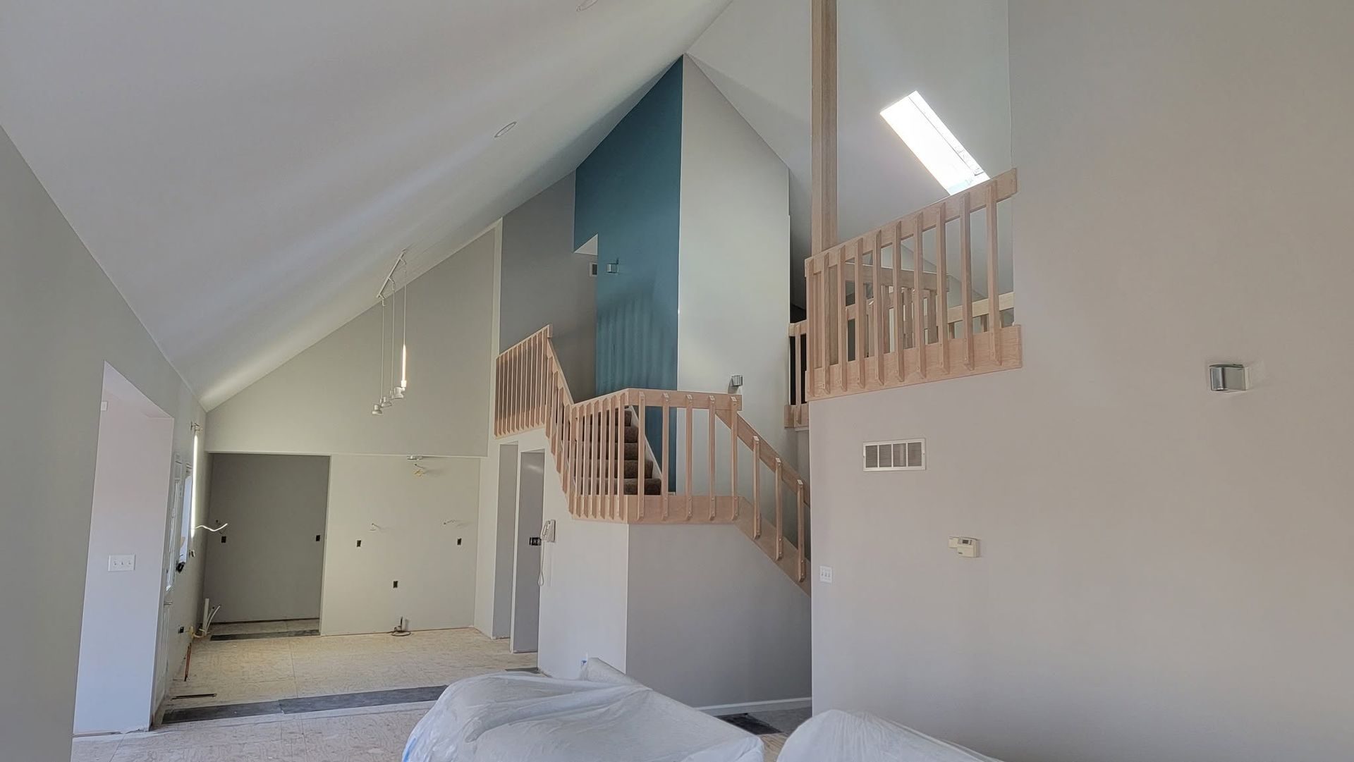 Modern loft interior with white walls, blue accent wall, curved wooden staircase, and skylight.