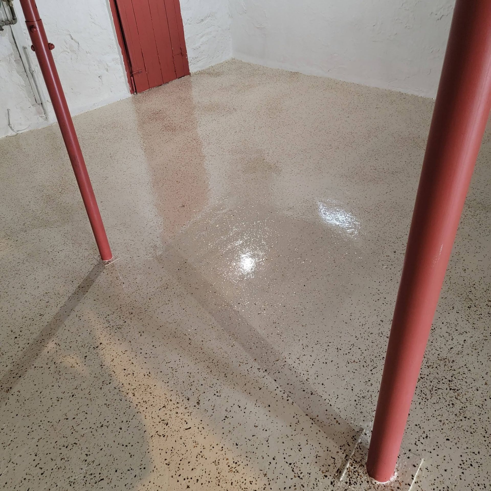 Shiny speckled terrazzo floor beside red-painted metal railings and a door