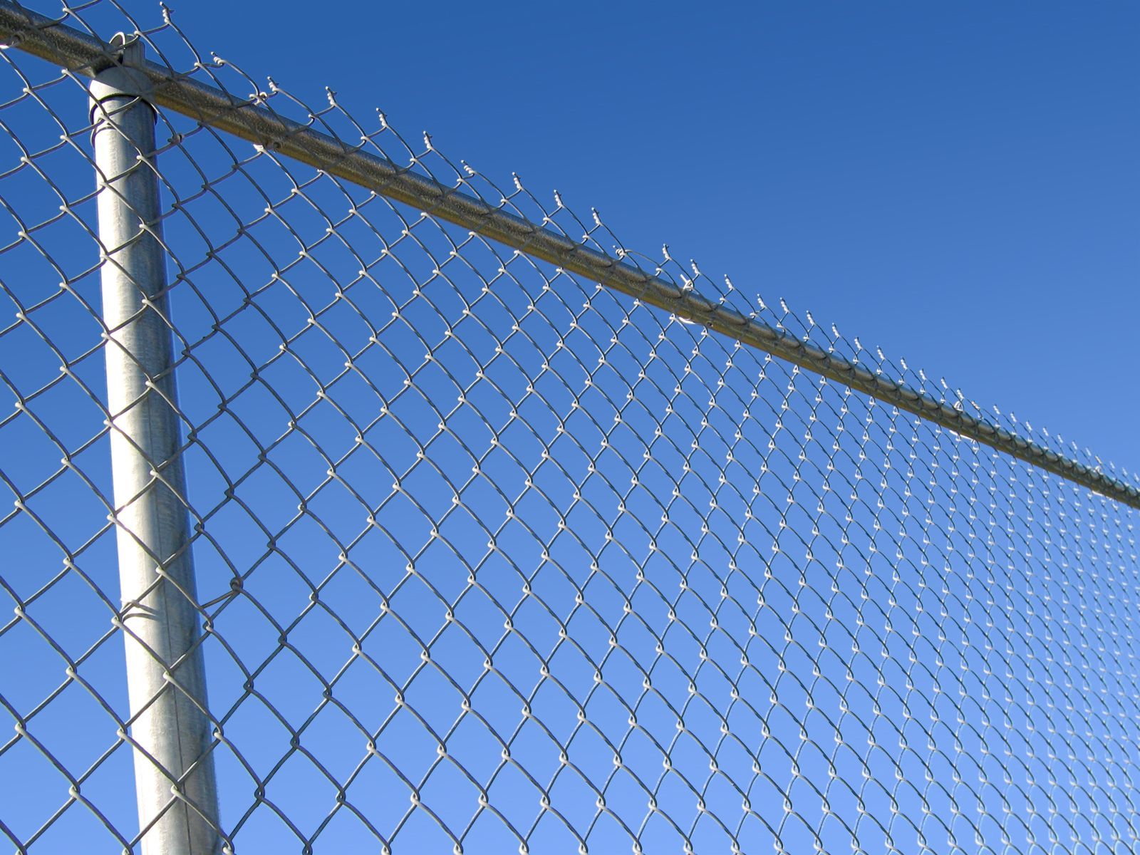 A chain link fence with barbed wire against a blue sky
