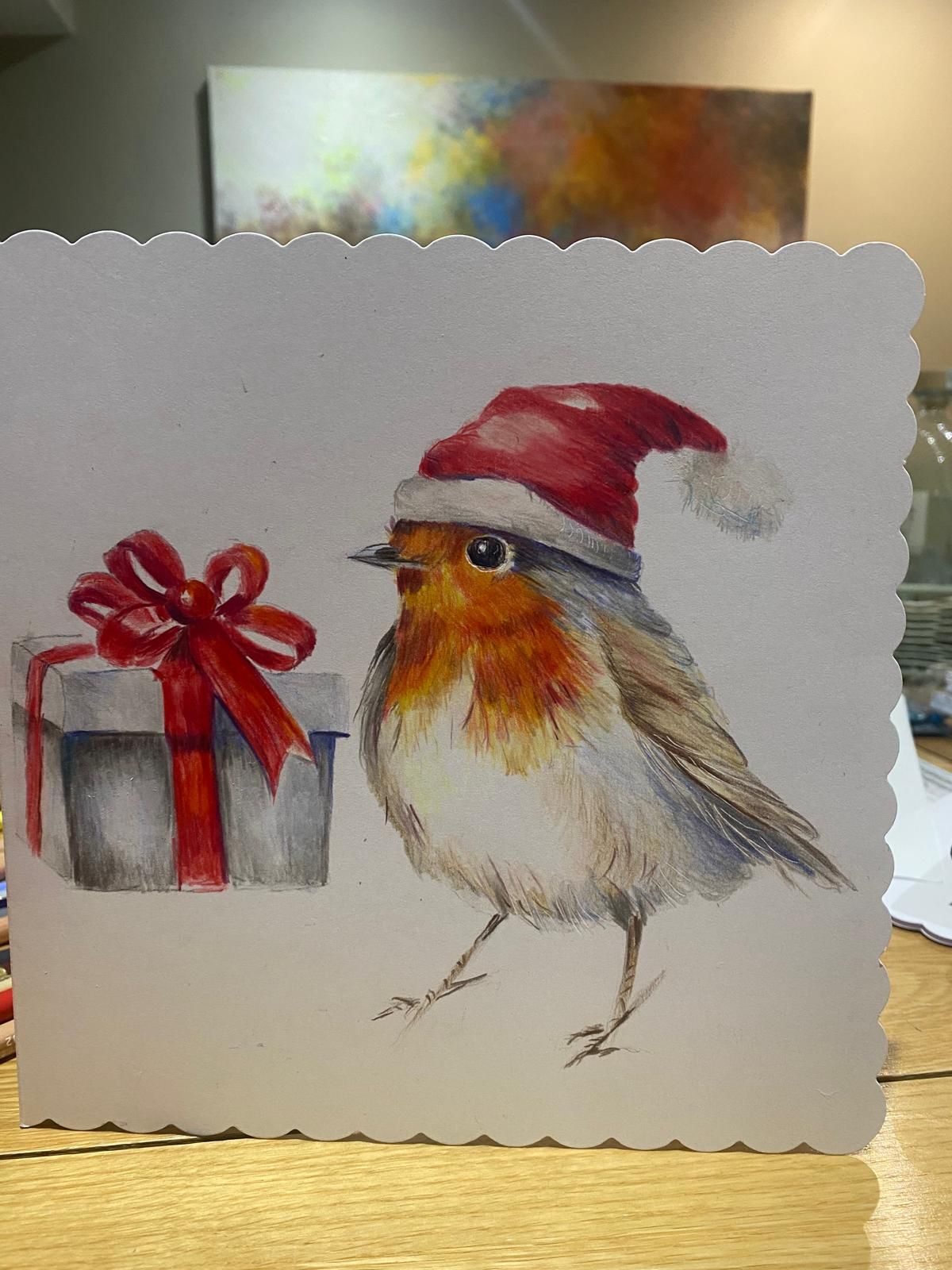 Christmas card: Robin wearing a Santa hat next to a wrapped present with a red bow.