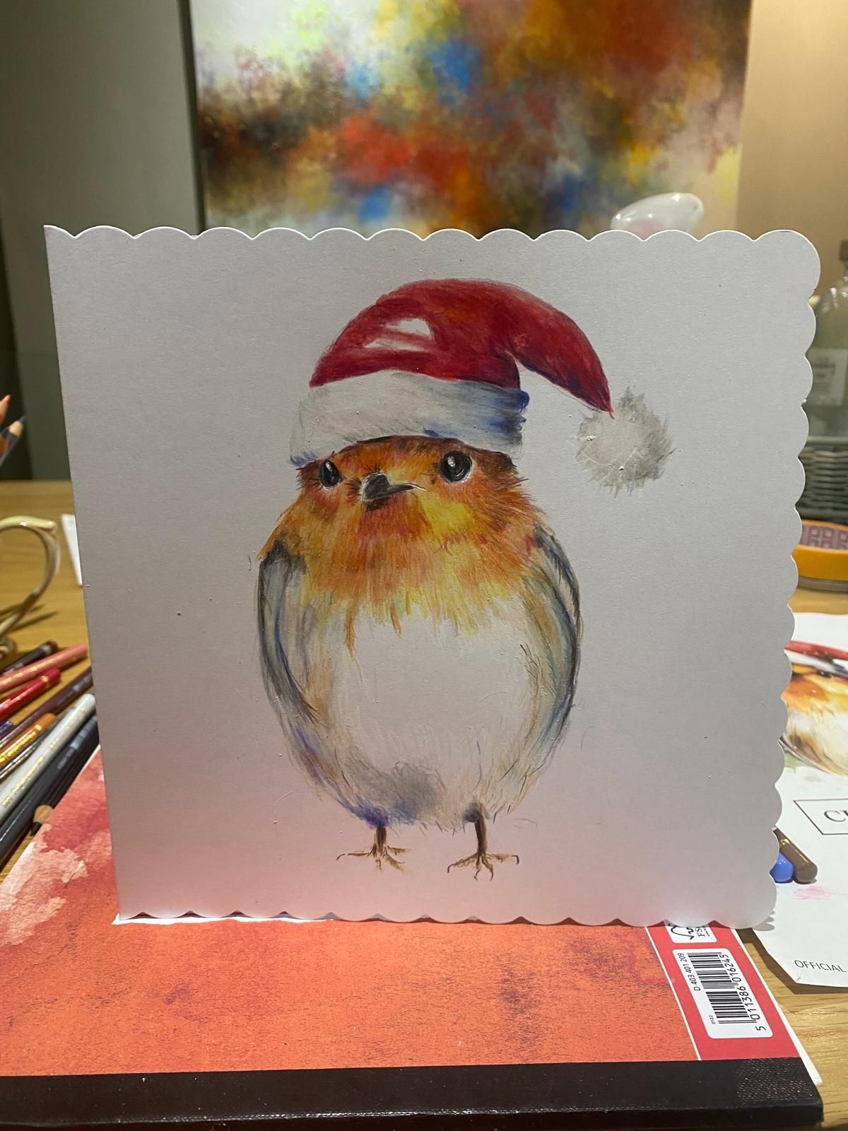 A watercolor painting of a robin wearing a Santa hat on a greeting card.