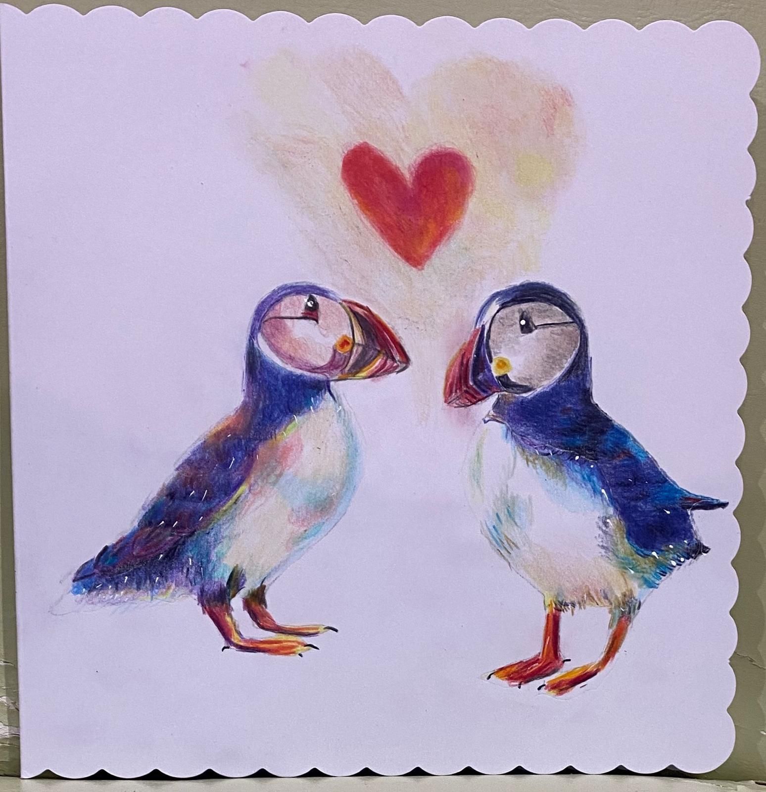 Two puffins gazing at each other beneath a red heart, surrounded by a light pink glow.