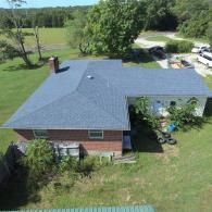 Overhead view of house with blue roof, trees, and green grass.