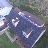 Rooftop with shingles under construction, visible windows, and building materials.