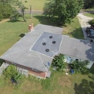 Aerial view of a house with an asphalt shingle roof and a flat section with tires on it.