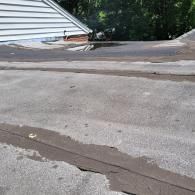 Flat roof with standing water, adjacent to a white-sided building with a brick chimney.