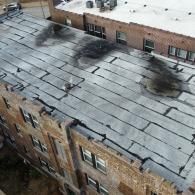 Building with a flat, dark roof showing several large, black scorch marks; aerial view.