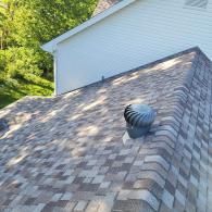 Close-up of a shingled roof with a spinning ventilation turbine. Sunlight casts shadows.