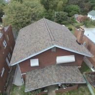 Overhead view of a house with a brown shingle roof, surrounded by trees and other buildings.