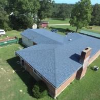 Blue shingle roof on a brick house with a chimney, green yard, and surrounding trees.