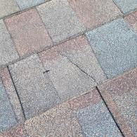 Close-up of asphalt roof shingles with a crack and small damage.