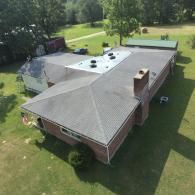 Overhead view of a brick building with a gray roof and several vents. A green lawn surrounds the structure.