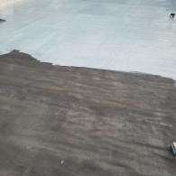 Dark gray ground surface, partially covered by light gray coating, outdoors.