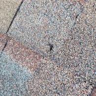 Close-up of weathered asphalt roof shingles in shades of gray, brown, and red.